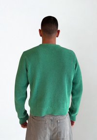 Zielony sweter z prążkowanego dzianiny z okrągłym dekoltem, z długimi rękawami i krótkim końcem. Wykonany z teksturowanej tkaniny, ma dopasowany krój.