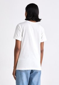 Biała bawełniana koszulka z klasycznym okrągłym dekoltem, kr�ótkimi rękawami i luźnym krojem, zestawiona z wyblakłymi niebieskimi dżinsami. Gładka tekstura, prosty design.