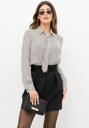 Blusa a fantasia bianca e nera con colletto aderente, abbinata a pantaloncini neri a vita alta. Accessoriata con pochette nera e occhiali da sole.