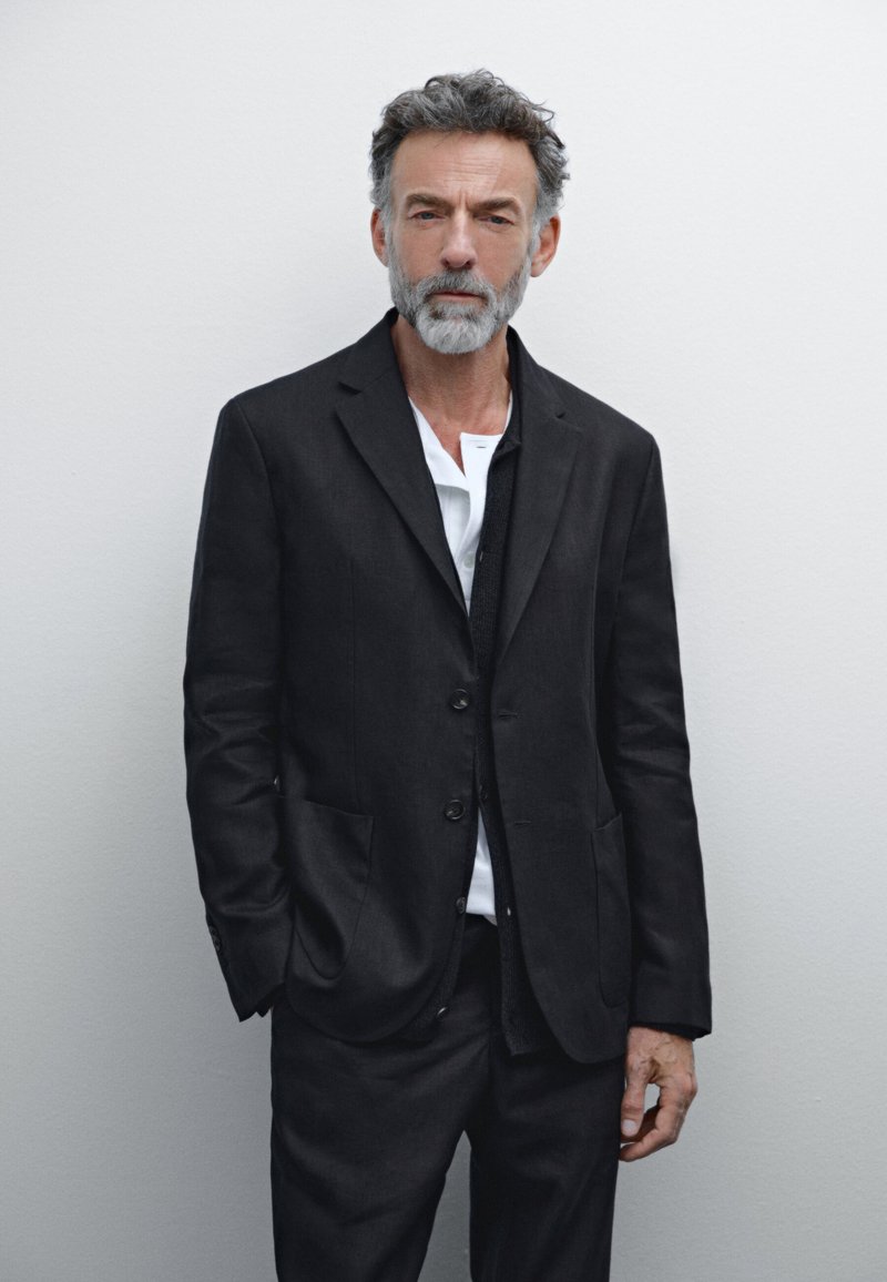 Schwarzer Leinenanzug mit einem taillierten Blazer und passenden Hosen. Der Blazer hat ein einreihiges Design, zwei Taschen und ein weißes Hemd darunter.
