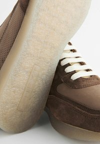 Brune sneakers med ruskind og mesh-stof, cremefarvede snørebånd og transparente gummisåler med præget branding.
