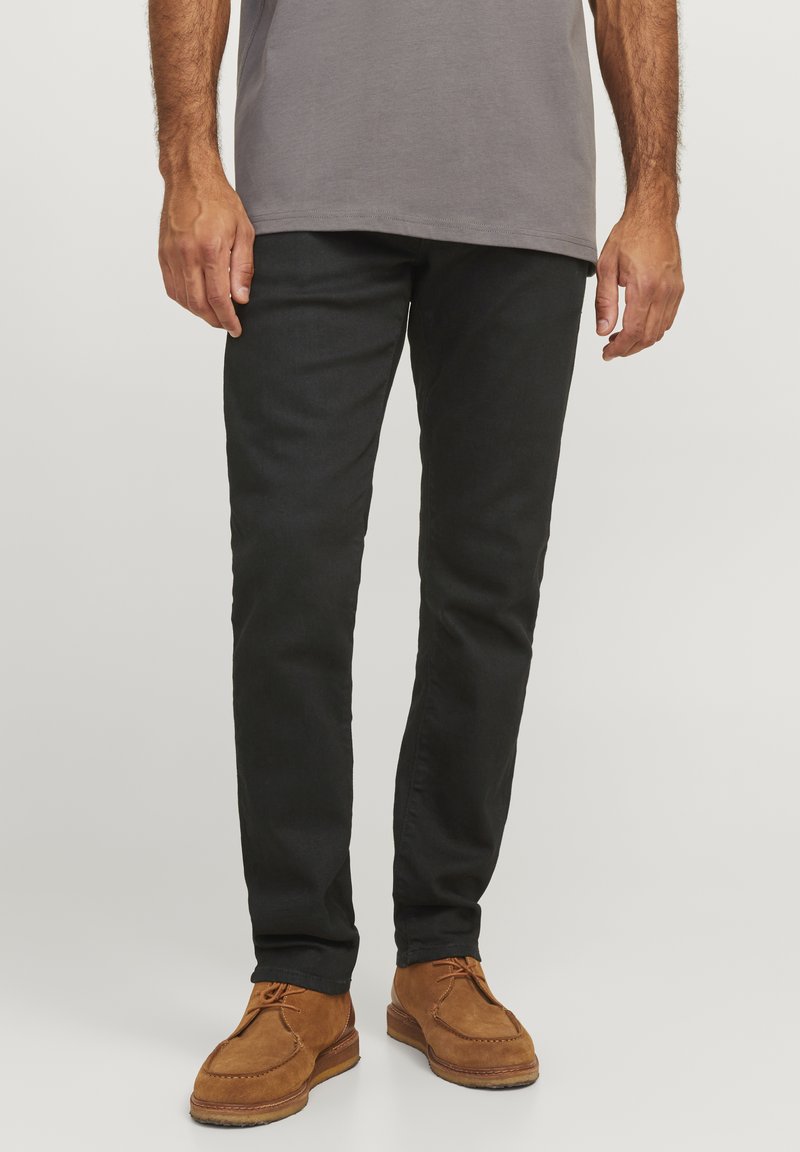 Jeans negros ajustados con una textura suave, acompañados de zapatos de ante marrón con un acento cosido y cordones.