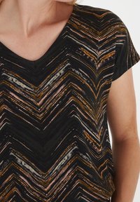 Černý top s krátkými rukávy, který má chevron vzor v oranžové, růžové, šedé a bílé barvě. Design s výstřihem do V a texturovaná tkanina.