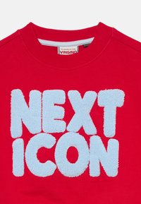 Červená mikina s modrým, nadýchaným písmom „NEXT ICON“ v tučnom písme a lemom na krku.