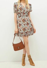 Floral print dress with puff sleeves, v-neckline, and ruffled hem. Worn with a brown handbag and lace-up tan heeled boots.
