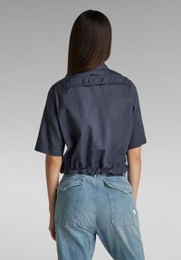 Marinblus med kort ärm i lätt material, med elastisk nederkant, i kombination med ljusblå, högmidjade jeans av denim med bakfickor.