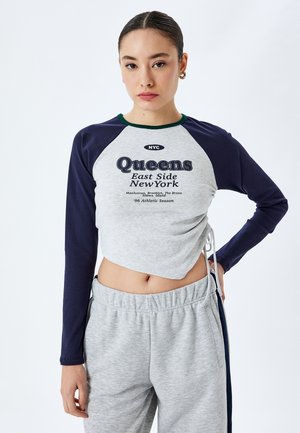 Grå og marineblå langærmet cropped skjorte med "Queens East Side New York" tryk, parret med lysegrå sweatpants med snor.