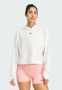 Weiße Kapuzenpullover mit einem cropped Design und langen Ärmeln, kombiniert mit hellrosa Sportshorts. Besitzt ein schwarzes Logo auf der Brust.