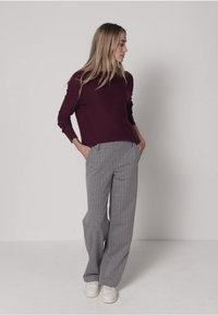 Pull bordeaux à manches longues associé à un pantalon large rayé vertical gris et des baskets blanches. Texture lisse et design décontracté.