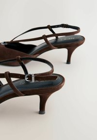 Ruskeat mokkasiinit slingback-korolla, jossa terävä kärki, ohuet hihnat ja hillitty hopeanvärinen solki. Varustettu piikkikorkoisella korolla ja kontrastivärisellä mustalla pohjallisella.