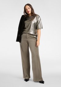 Metaliczna srebrna bluzka z krótkim rękawem zestawiona z beżowymi, szerokimi spodniami z wysokim stanem, uzupełniona czarną marynarką. Widoczne detale teksturowanego materiału.