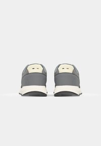 Chaussures de sport grises avec un talon crème contrastant. Semelle texturée et marque minimaliste à l'arrière. Design simple et moderne.