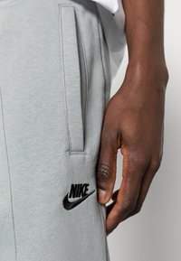 Gray cotton sweatpants feature side pockets and a black embroidered Nike logo. The fabric has a smooth, textured finish.