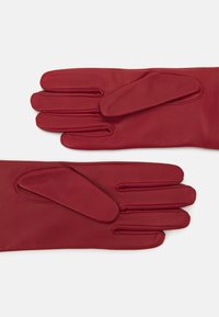 Guanti in pelle rossa con una texture liscia, design a cinque dita e polsino aderente con aperture decorative sulle dita.