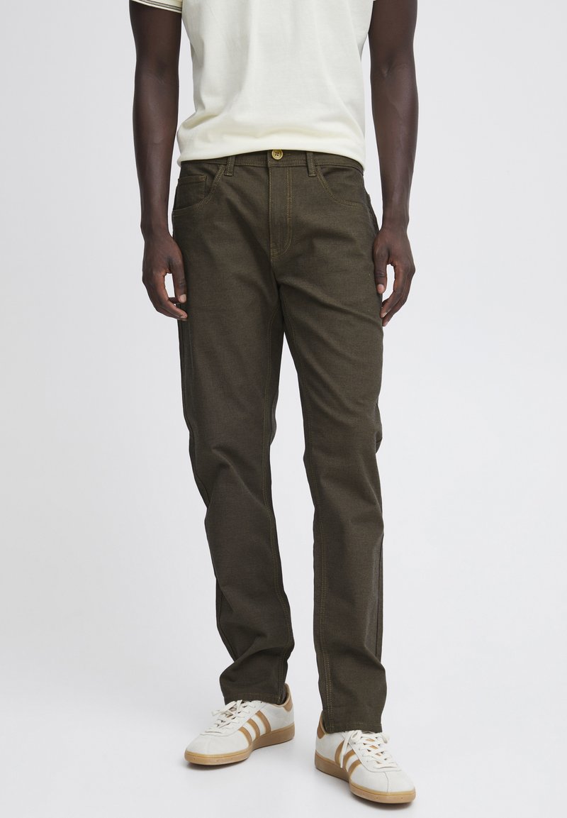 Pantalones de color verde oliva oscuro hechos de una tela texturizada, con un corte regular, cinco bolsillos y costuras en amarillo contrastante.