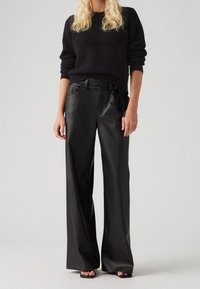 Szerokie czarne skórzane spodnie z wysokim stanem, z przednimi kieszeniami i detalem nawiązu. Połączone z fakturowanym czarnym swetrem wełnianym.