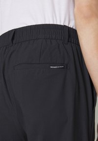 Čierne elastické nohavice v páse s jedným zadným vreckom. Tkanina je hladká a ľahká, s označením "DENIM TOM TAILOR."