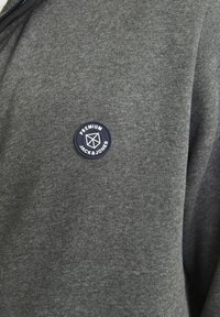 Sivá mikina na zips z mäkkého materiálu s okrúhlym modrým nášivkou a bielym textom "PREMIUM JACK & JONES."