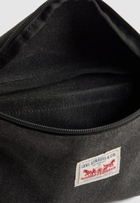 Schwarze Stofftasche mit einem offenen Reißverschluss, der ein leeres Innenleben zeigt, sowie einem Levi Strauss & Co. Logo-Patch auf der Vorderseite.