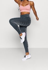 Růžová sportovní podprsenka Nike, šedé legíny se vzorem a vertikálními pruhy a detaily ve tvaru včelího plástu, doplněné bílými sportovními botami.