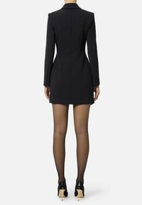 Abito nero su misura con maniche lunghe, silhouette aderente e spacco posteriore. Indossato con calze nere trasparenti e scarpe nere con tacco alto.