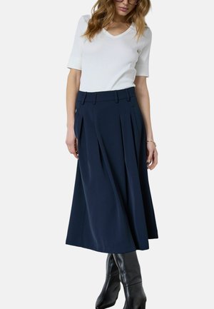 Jupe plissée bleu marine en tissu à texture lisse, dotée d'une taille élastique et de poches latérales. Assortie à un haut blanc à manches courtes.