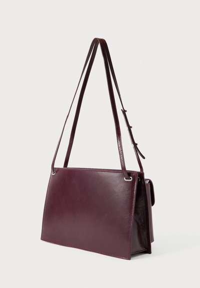 Σκούρα βουργουνδί δερμάτινη τσάντα ώμου με ορθογώνιο σχήμα, ρυθμιζόμενους διπλούς ιμάντες και μικρή πλαϊνή θήκη σε απλό φόντο.
