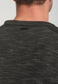 Pull en maille texturée gris foncé avec un col côtelé. Présente une petite étiquette de marque à l'arrière. Le tissu semble tricoté et légèrement rugueux.