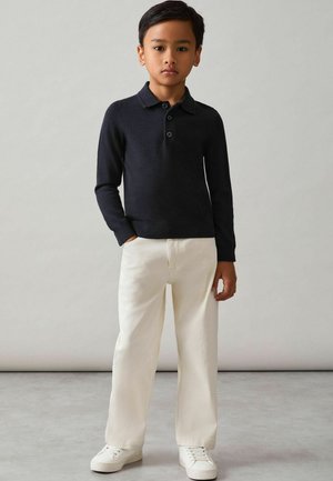 Must nümbriline polo, millel on kolm nööpi, kreemivärvi laiad püksid ja valged tossud. Sile tekstuur, juhuslik disain, nähtavad mustrid puuduvad.