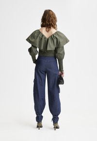 Top verde scollato con grandi maniche voluminose, abbinato a pantaloni cargo in denim blu e tacchi verde scuro. Borsa nera in mano.