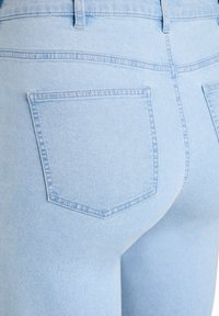 Svetlomodré rifle z denimu s priliehavým strihom, obsahujúce dve zadné vrecká a viditeľné švy. Hladká textúra a upravený tvar.