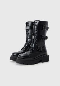 Black leather ankle boots with multiple straps and buckles, round toe, and chunky rubber sole; features eyelets and contrasting texture.