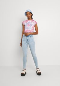 Kuttet t-skjorte med batikk i rosa og lavendel med blomsterdesign, sammen med lyseblå skinny jeans og svarte platåsandaler. Blå bøttehatt.