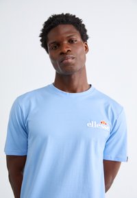 Light blue t-shirt made of soft cotton, featuring a round neckline and short sleeves, with a white embroidered logo on the chest.