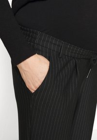 Sorte pinstripede bukser med elastisk talje og sidelommer. Stoffet ser glat og let ud.