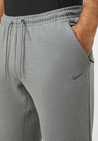 Gray sweatpants with an elastic waistband, drawstring, and side pockets. Features a small black Nike logo on the left thigh. Soft fabric texture.