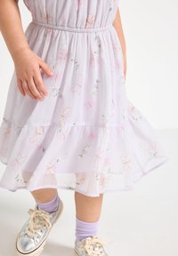 Robe fleurie violet clair avec jupe à plusieurs couches. Présente des motifs de papillons et de fleurs roses. Tissu doux et texturé, avec une taille élastique.