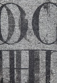 Szary materiał z błyszczącym czarnym tekstem o różnych rozmiarach czcionki. Tekstura wydaje się dzianinowa z subtelnym efektem migotania na całej powierzchni.