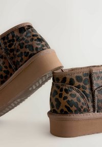 Korte støvler i leopardmønstret faux pels med en brun gummisål. Har en stikning langs kanten og en blød tekstur. Flad, rund form.