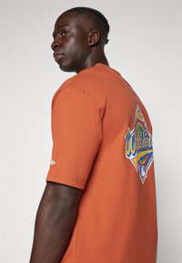 Oranje katoenen T-shirt met korte mouwen, met een kleurrafische "World Series" op de achterkant en een logo op de mouw.