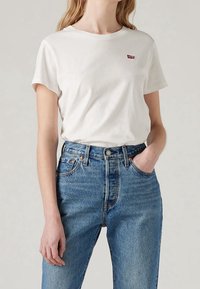Hvid bomulds T-shirt med korte ærmer og et lille rødt Levi's-logo på brystet, parret med højtaljede blå denimjeans.