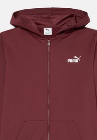 Burgundijas krāsas kapuci ar rāvējslēdzēju, izgatavots no gludas auduma. Iekļauj priekšējos kabatas un baltu Puma logo kreisajā krūtis.