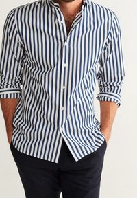 Camicia a righe in navy e bianco. Presenta una chiusura con bottoni sul davanti, maniche lunghe e colletto a punte, con una forma aderente e una texture liscia.
