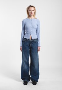 Ljusblå ribbad långärmad topp med framknäppning, tillsammans med vida mörkblå denimjeans och svarta skor.