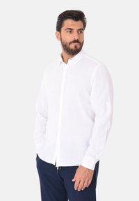 Camicia bianca a maniche lunghe in tessuto leggero con abbottonatura frontale, colletto a punta e polsini cuciti, abbinata a pantaloni blu navy.