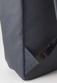 Angolo di uno zaino in tessuto grigio con una superficie testurizzata, cuciture rinforzate e una tracolla regolabile per una chiusura sicura.