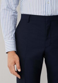 Pantalons bleu marine avec une texture lisse, dotés de poches latérales et d'une coupe droite, associés à une chemise à rayures bleu clair et blanche au niveau des poignets.