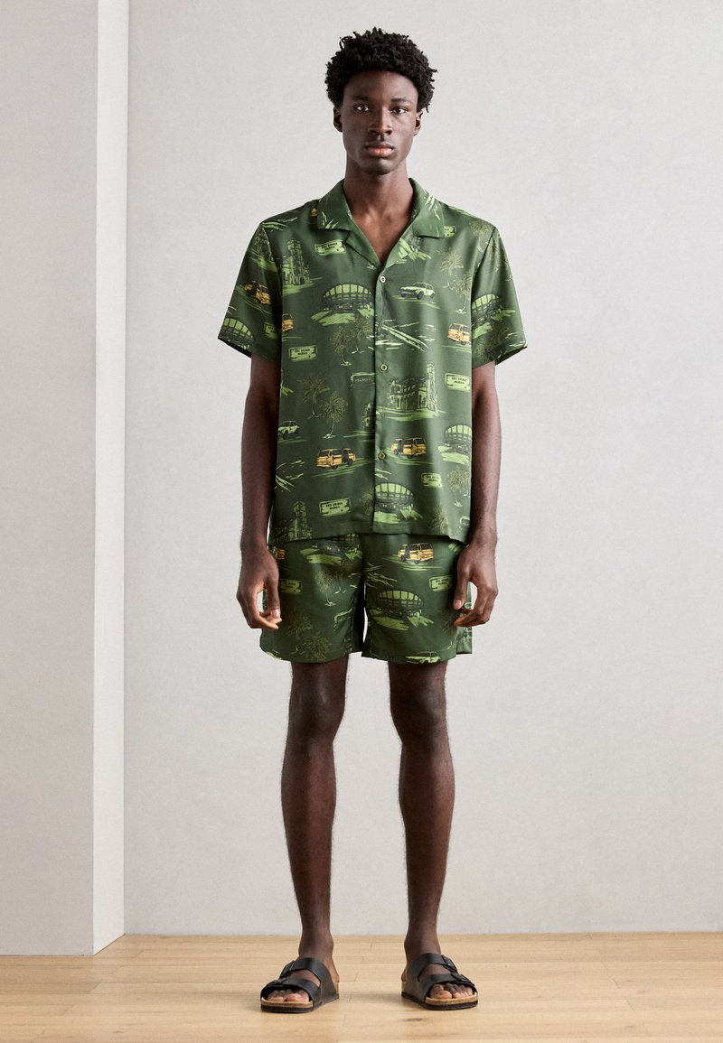 Grøn kortærmet skjorte og matchende shorts med et vintage print af køretøjer og landskaber. Letvægtsstof med en afslappet pasform.