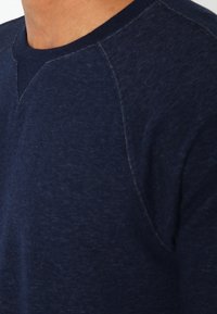 Sudadera de cuello redondo en azul marino con una tela texturada y detalles de costura contrastantes alrededor del escote y los hombros.