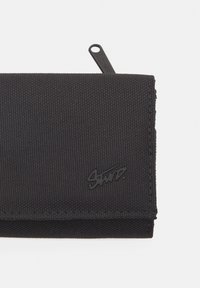 Black wallet made of textured fabric, featuring a fold-over design. Includes a zip pull and a subtle branded logo on the front.